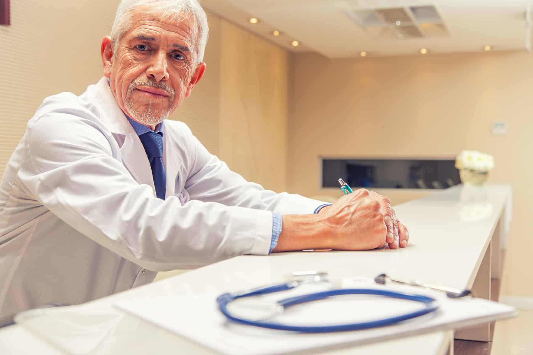 Doctor looking at camera with stethoscope on the table in front of him