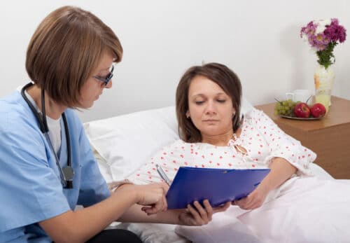 Woman in bed while looking at nurses clipboard
